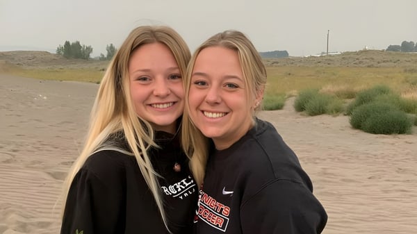 Zwei lächelnde Schülerinnen stehen in der Wüstenlandschaft mit Straßen und Sträuchern auf dem Gelände der Hillcrest High School.