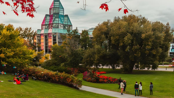 Im herbstlichen Park vor dem bunten Schulgebäude der Hillcrest High School spazieren Menschen zwischen farbigen Bäumen.