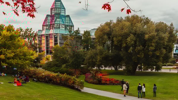 Im herbstlichen Park vor dem bunten Schulgebäude der Hillcrest High School spazieren Menschen zwischen farbigen Bäumen.