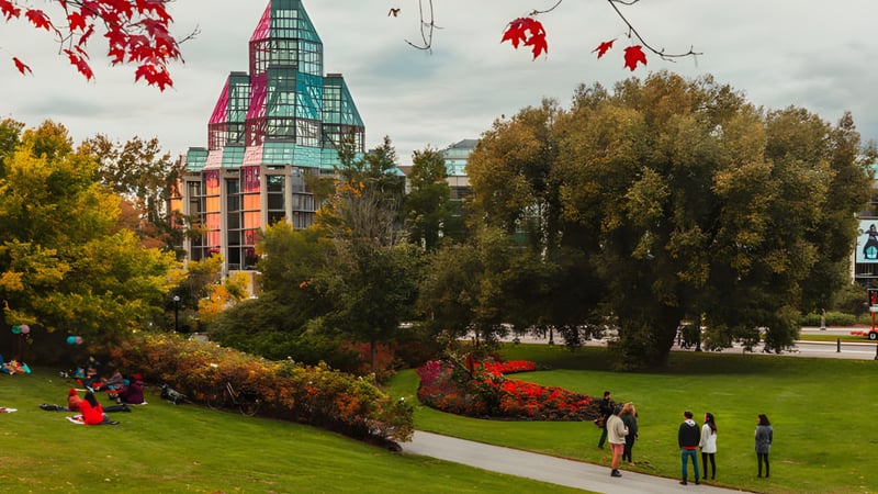 Im herbstlichen Park vor dem bunten Schulgebäude der Hillcrest High School spazieren Menschen zwischen farbigen Bäumen.