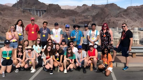 Eine Gruppe von Schülerinnen und Schülern der Hillcrest High School posiert vor einer dramatischen Berglandschaft mit einer Brücke im Hintergrund.