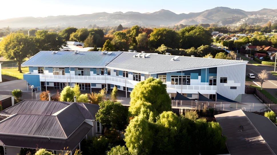 Das moderne mehrstöckige Gebäude der Hillmorton High School steht umgeben von grüner Landschaft mit Bergen im Hintergrund.
