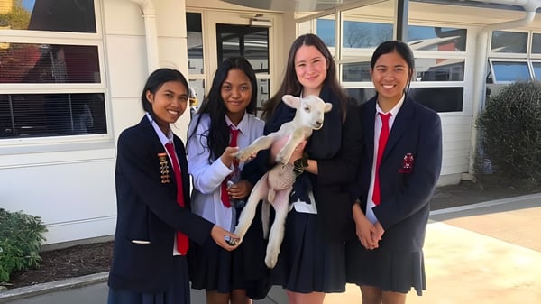 Vier Schülerinnen in Schuluniformen stehen vor dem Gebäude der Hillmorton High School und lächeln in die Kamera.