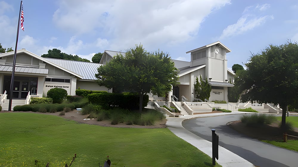 Das gut gepflegte Gebäude der Hilton Head Preparatory School mit Metall-Dach und hohem Schornstein steht auf einer Grasfläche neben einem gepflasterten Weg.