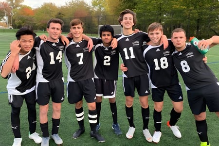 Eine Gruppe junger Fußballspieler in schwarzen Trikots posiert auf dem Sportfeld der H.J. Cambie Secondary School.
