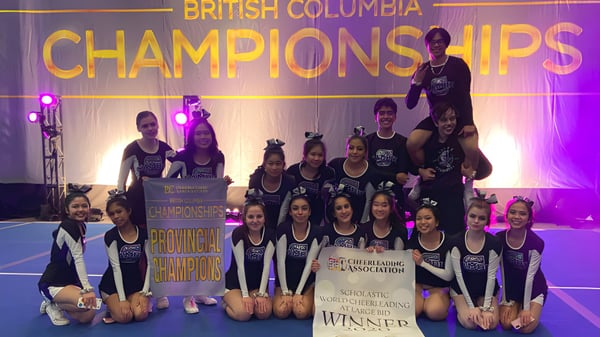 Eine Gruppe junger Turner der H.J. Cambie Secondary School posiert gemeinsam auf der Bühne vor einem Banner der British Columbia Championships.