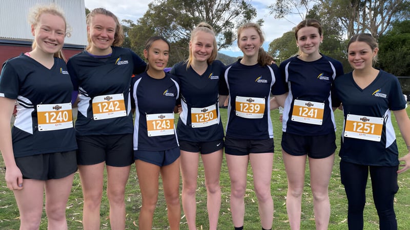 Eine Gruppe junger Athletinnen steht auf dem Campus der Hobart City High School vor einem bewaldeten Hintergrund.