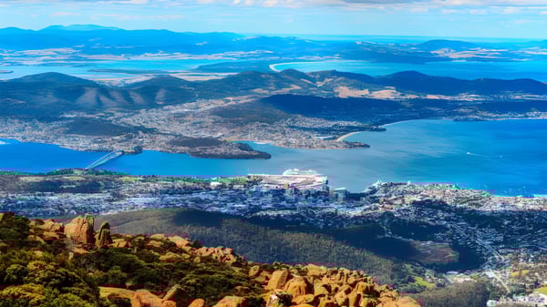 Luftaufnahme einer Küstenstadt mit Bergen und Wasser in der Nähe der Hobart City High School.