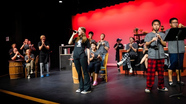 Schüler der Holderness School stehen mit Musikinstrumenten auf einer Bühne vor rotem Hintergrund.