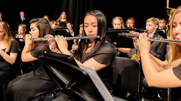 Schüler der Holland Christian Schools spielen Blasinstrumente auf einer Bühne mit dunklem Hintergrund.
