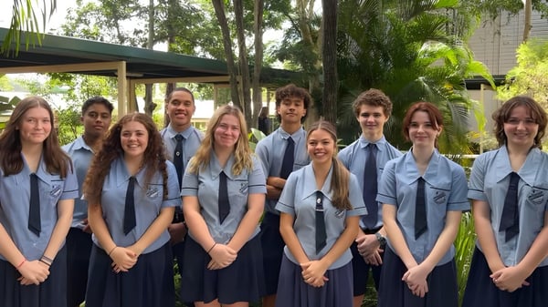 Eine Gruppe von Schülerinnen und Schülern der Holland Park State High School steht zusammen in einem grünen Außenbereich mit Bäumen und Schulgebäuden im Hintergrund.