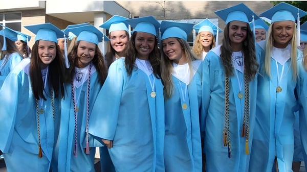 Eine Gruppe von Absolventinnen und Absolventen der Holland Park State High School steht in blauen Talaren vor einem Gebäude und feiert ihren Abschluss.