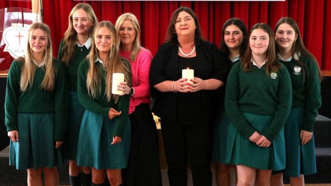 Eine Gruppe Schülerinnen in grünen Schuluniformen steht vor einem roten Vorhang auf dem Campus der Holy Child Secondary School, eine Schülerin hält eine brennende Kerze.