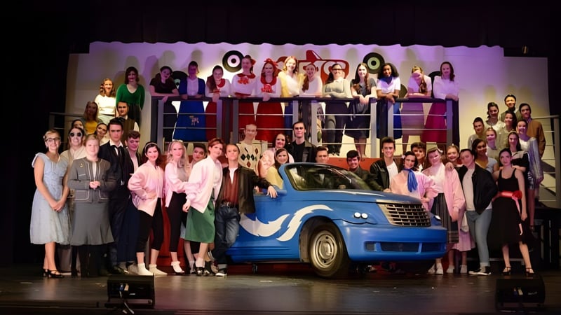 Eine Gruppe von Schülern der Holy Cross Catholic Secondary School steht auf einer Bühne vor einem blauen Auto mit einem grafischen Hintergrund.