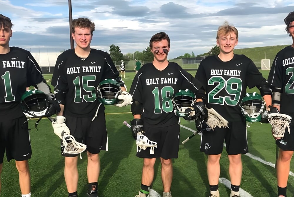 Eine Gruppe Schüler der Holy Family Catholic High School steht in einheitlichen Trikots auf einem Sportfeld vor bewölktem Himmel.