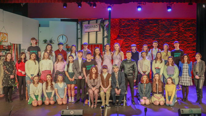 Eine Gruppe Schülerinnen und Schüler steht auf der Bühne des Holy Rosary College vor einer Wand aus Backsteinen bei farbiger Beleuchtung.
