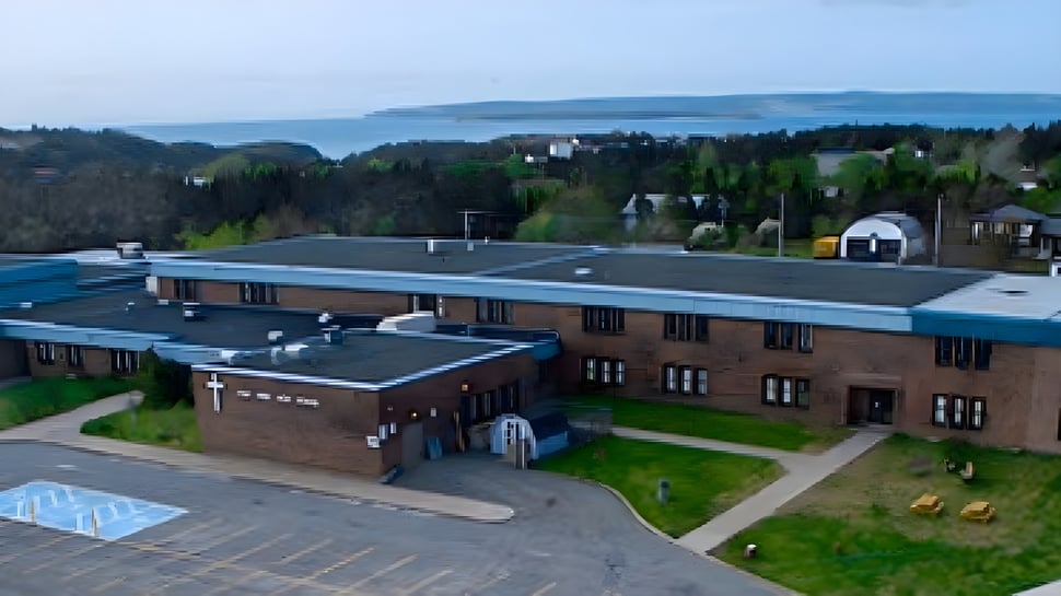 Das mehrstöckige Backsteingebäude der Holy Spirit High School steht auf einem grasbewachsenen Campus mit Blick auf ein Gewässer.