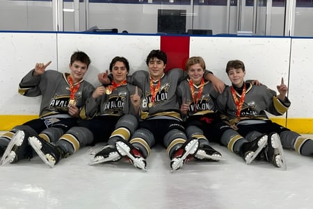 Eine Gruppe junger Hockeyspieler sitzt in Uniform auf dem Eis auf der Eisfläche der Holy Spirit High School.