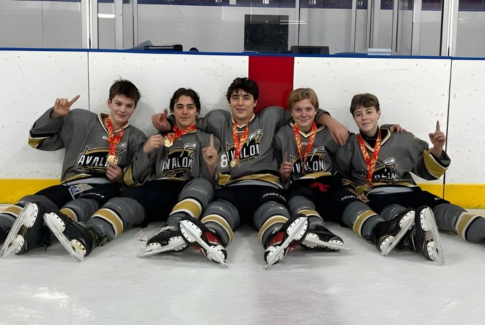 Eine Gruppe junger Hockeyspieler sitzt in Uniform auf dem Eis auf der Eisfläche der Holy Spirit High School.