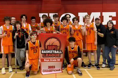 Eine Gruppe junger Basketballspielerinnen und -spieler der Holy Trinity High School hält in der Turnhalle gemeinsam einen Meisterschaftspokal.