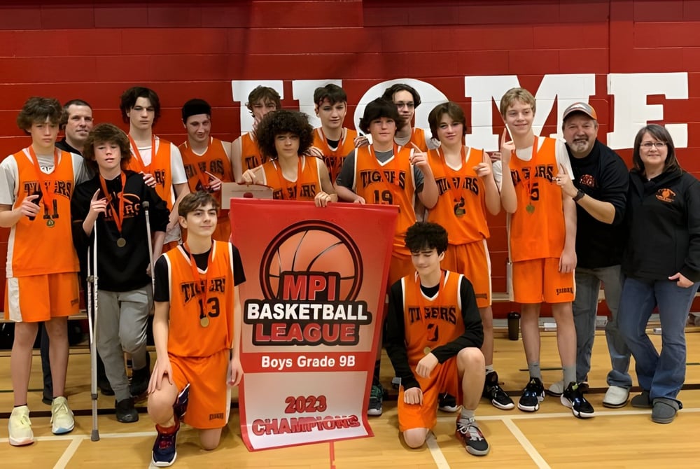 Eine Gruppe junger Basketballspielerinnen und -spieler der Holy Trinity High School hält in der Turnhalle gemeinsam einen Meisterschaftspokal.