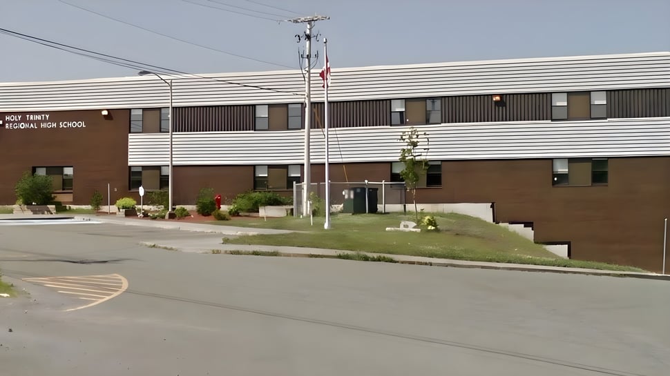 Das mehrstöckige Gebäude der Holy Trinity High School mit brauner Fassade steht umgeben von einer Grünfläche und einer Straße im Vordergrund.