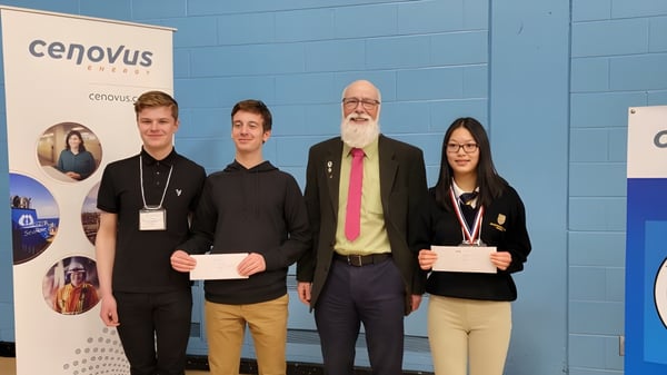 Vier Personen stehen vor einer blauen Wand mit dem Cenovus Logo auf einer Veranstaltung der Holy Trinity High School.