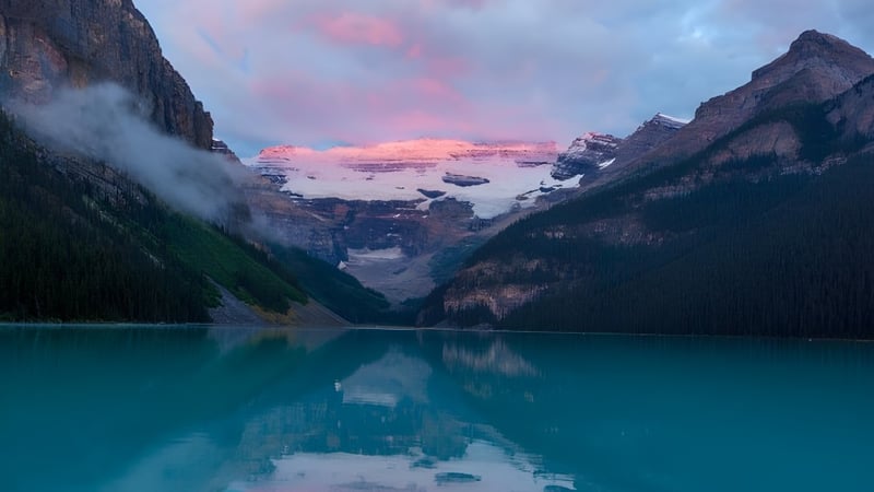 Ein Bergsee in den Alpen spiegelt bei Sonnenuntergang die schneebedeckten Gipfel wider.