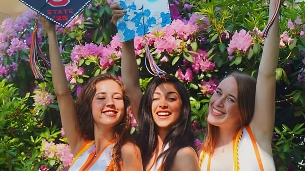 Drei Schülerinnen der Hopkinton High School posieren vor einem farbenfrohen Blumen-Hintergrund.