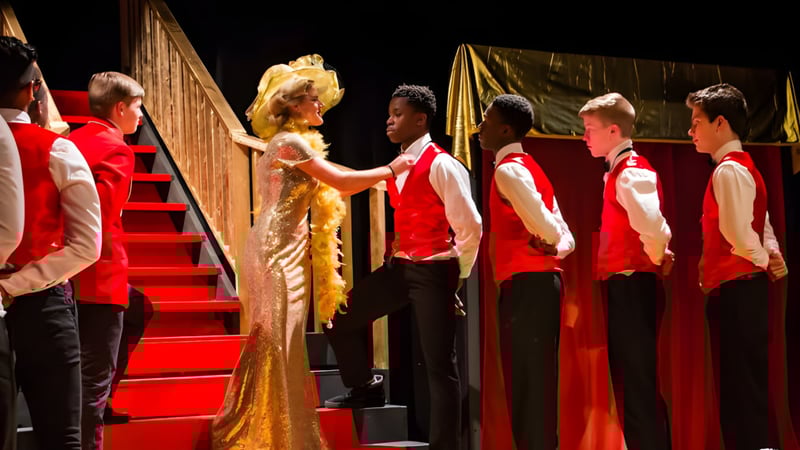 Schüler der Houghton Academy tragen bei der Abschlussfeier rote Talare auf einer Bühne mit goldenem Vorhang.