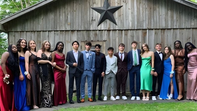 Eine Gruppe in formeller Kleidung steht vor einer rustikalen Scheune mit großem Stern auf dem Campus der Houghton Academy.