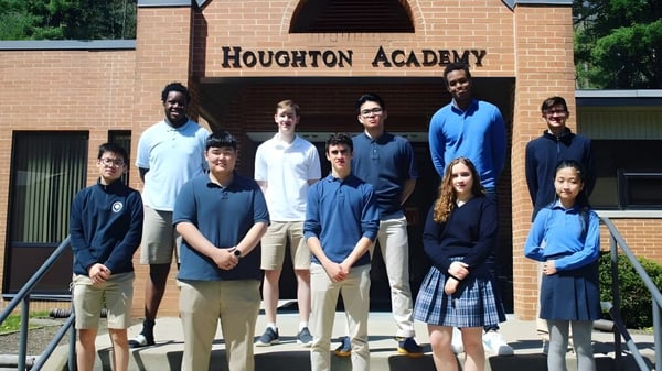 Eine Gruppe Schüler steht vor dem Gebäude der Houghton Academy in Schuluniformen und posiert für ein Foto.