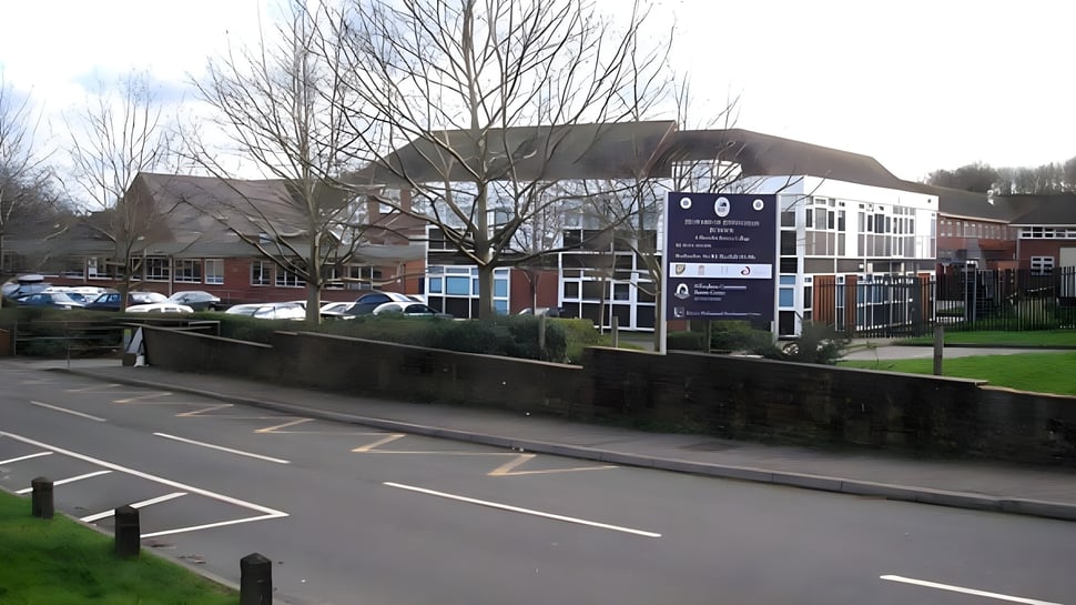 Das mehrstöckige Gebäude mit Glaseingang der Howard of Effingham School ist von kahlen Bäumen und einem Parkplatz umgeben.