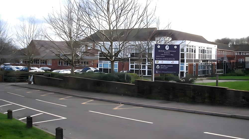 Das mehrstöckige Gebäude mit Glaseingang der Howard of Effingham School ist von kahlen Bäumen und einem Parkplatz umgeben.