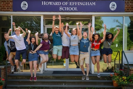 Eine Gruppe von Schülerinnen und Schülern steht mit erhobenen Armen vor der Howard of Effingham School und feiert.