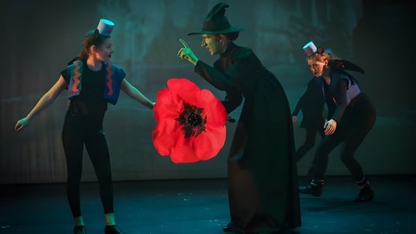 Theateraufführung mit Schülerinnen und Schülern der Howard of Effingham School, eine Person trägt schwarzen Umhang und Hut, eine große rote Mohnblume ist im Vordergrund sichtbar.