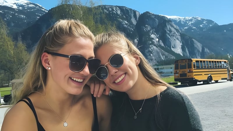Zwei Schülerinnen mit blonden Haaren posieren vor einer Berglandschaft auf dem Gelände der Howe Sound Secondary School.