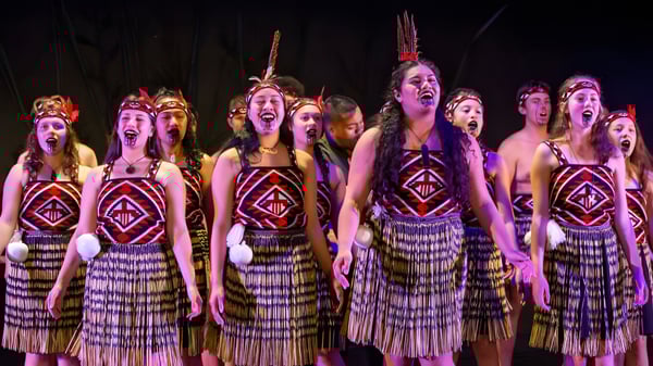 Eine Gruppe von Schülerinnen und Schülern des Howick College steht in bunten Kostümen auf der Bühne und singt gemeinsam.