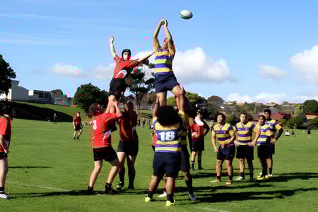 Eine Gruppe Schüler spielt Rugby auf dem Sportplatz des Howick College vor Gebäuden und Bäumen.