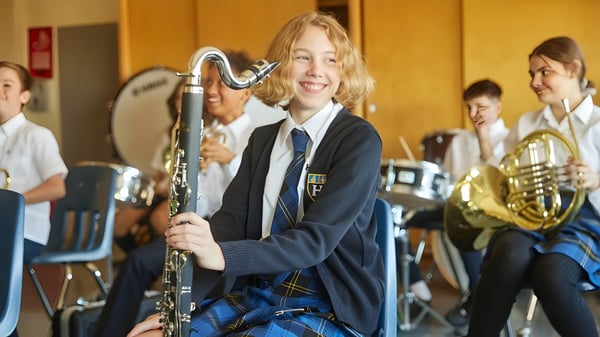 Ein Schüler des Hudson College spielt begeistert ein Musikinstrument im Musikunterricht mit anderen Schülern im Hintergrund.