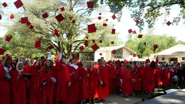 Eine Gruppe von Schülerinnen und Schülern der The Hun School of Princeton steht in roten Abschlussgewändern unter Bäumen mit roten Dekorationen.