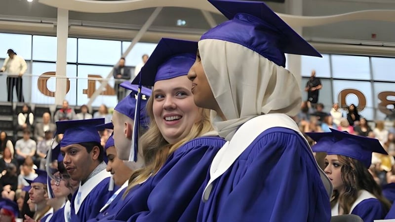 Eine Gruppe von Absolventinnen und Absolventen der Hunting Hills High School trägt lila Abschlussgewänder und Hüte in einem vollen Auditorium.