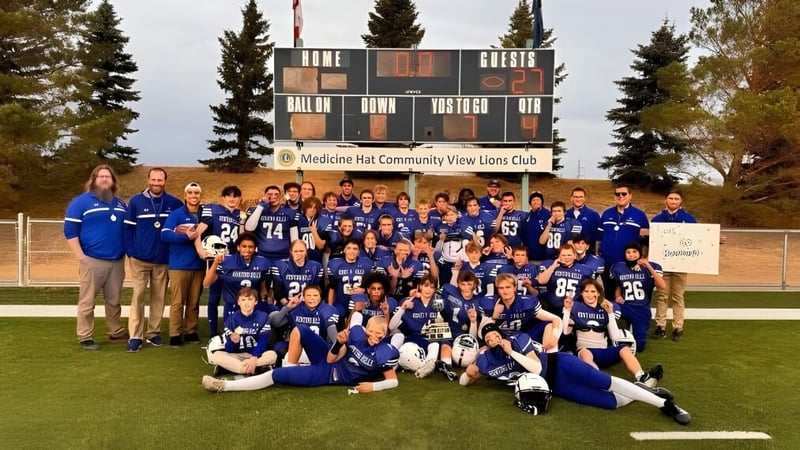 Die Sportmannschaft der Hunting Hills High School steht gemeinsam vor einer Anzeigetafel im Freien mit Kiefern im Hintergrund.