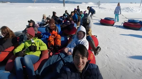 Eine Gruppe von Schülerinnen und Schülern der Huntington High School sind in Winterkleidung auf einem schneebedeckten Hang mit einem Skilift im Hintergrund versammelt.