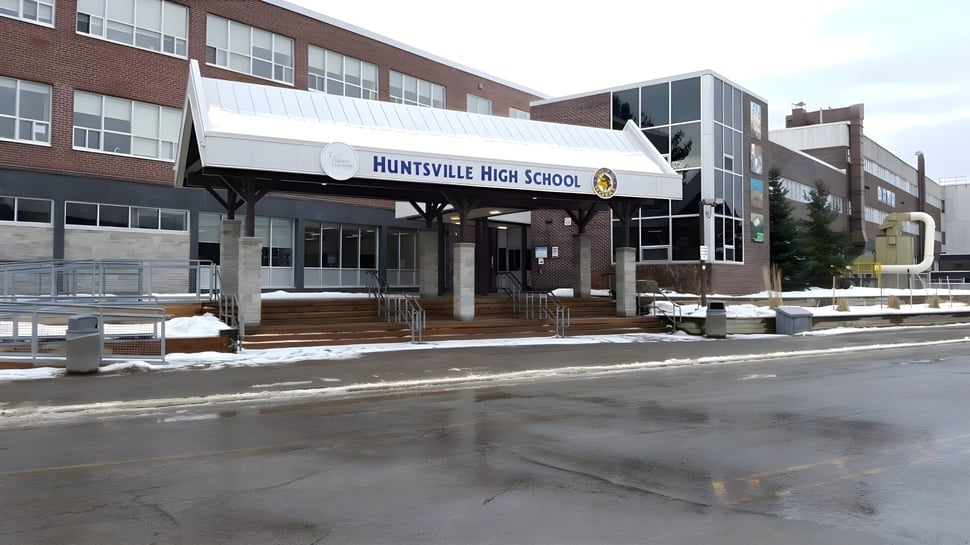 Das große Backsteingebäude der Huntsville High School steht eingebettet in eine verschneite Landschaft unter einem bewölkten Himmel.