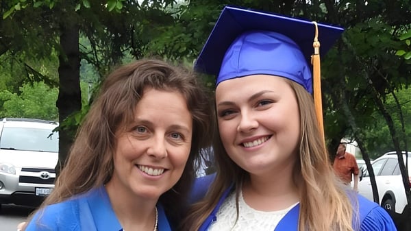Zwei Frauen, eine mit Absolventenhut, stehen zusammen vor bewaldetem Hintergrund auf dem Campus der Huntsville High School.