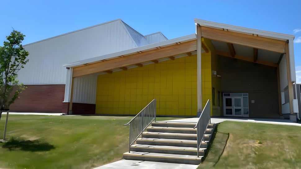 Das moderne mehrstöckige Gebäude der Huntsville School mit gelber Fassade und überdachtem Eingang umgeben von Grünfläche und Bäumen.