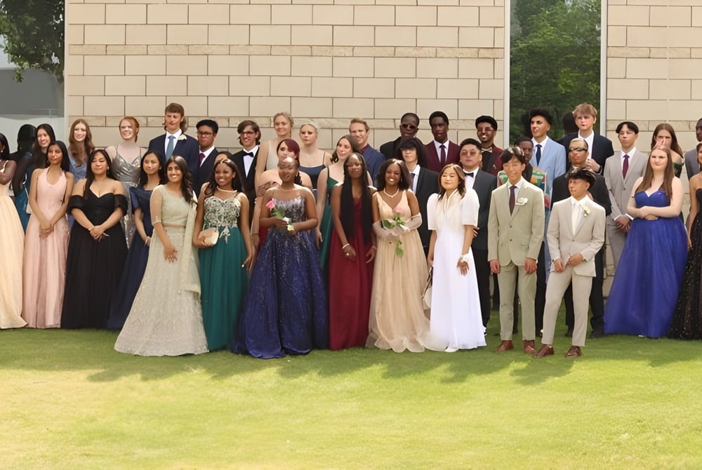 Eine große Gruppe von Schülerinnen und Schülern der Huntsville School steht in formeller Kleidung auf einer Wiese vor einem Backsteingebäude.