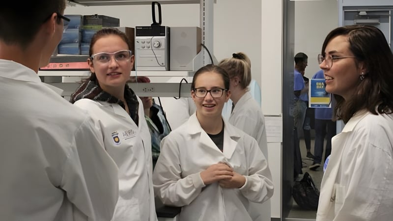 Schüler der Huntsville School unterhalten sich in weißen Laborkitteln in einem Laborraum.