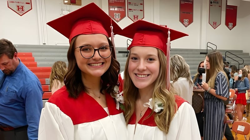 Zwei Schülerinnen tragen rote Abschlussmützen und -roben und posieren in der Huron High School neben Dekorationen zur Abschlussfeier.